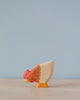 A high-quality Handmade Holzwald Hen painted in natural tones of white, orange, and red, stands against a soft blue background.