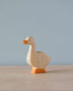 A sustainable Handmade Holzwald Goose figurine with a light body and orange beak and feet, standing against a soft blue background.
