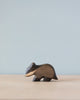 A Handmade Holzwald Badger figurine standing on a plain surface with a soft blue background. This sustainable toy highlights natural wood grains and a smooth finish.