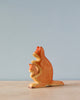 A Handmade Holzwald Kangaroo With Baby figurine stands on a flat surface against a soft blue background. The figurine, representing sustainable toys, is intricately carved, depicting the kangaroo with her baby in a sitting pose.
