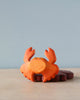 A high-quality Handmade Holzwald Crab toy with prominent eyes painted on, resting on a plain surface against a soft blue background. The crab is in an open stance with its claws raised.