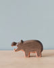 A Handmade Holzwald Hippo figurine on a smooth surface with a pale blue background. The figurine, representing sustainable toys, is crafted with visible details such as eyes and ears and has a natural wood