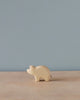 A handmade Holzwald Piglet figurine on a wooden surface against a plain light blue background. The figurine is minimalistic with visible wood grains and represents sustainable toys.