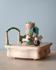 The Unicorn Music Box is a hand-cranked music box with a small unicorn, white horse, castle tower, green archway, and trees on a light wood base against a pale blue background.