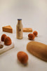A minimalist still life arrangement featuring a small, Sabo Concept Handmade Wooden Dairy Set surrounded by wooden objects including educational toys, a spoon, and geometric shapes on a soft beige background.