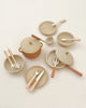 Handmade Wooden Kitchen Essentials - Flower featuring a large pot with handles and lid, three smaller pans with lids and long handles, two plates, a bowl, and various utensils including spoons, spatulas, forks, and knives—all laid out on a light surface. These handmade kitchen toys are crafted from non-toxic paint wooden toys.