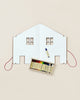A creative flat lay featuring a white cardboard cutout of The Dollhouse Drawing Book split in half, with a red thread outlining its perimeter, and a box containing colorful thread spools placed beneath it, alongside a drawing