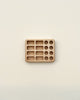A minimalist image showcasing a Crayon Tray For Stockmar - 8 x 8 Slots with various sized compartments, each containing a different number of cylindrical Linden wood pieces, arranged on an off-white background.