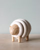 A Lacing Wooden Sheep with a simplistic design, featuring layered rings for its body and small, round head with minimal features, standing on a light surface against a soft blue background.