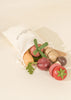 Sliceable wooden vegetable toys spilling out of a cotton bag.