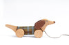 The Handmade Pull Along Dog Toy is shaped like a dachshund with large round wheels, a plaid body midsection painted with natural milk paint, and a string attached to its nose, set against a plain.
