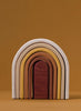 A stack of Raduga Grez Handmade Wooden Oval Rainbow Stackers made from non-toxic linden wood, arranged to form a single, curved structure against a plain brown background.